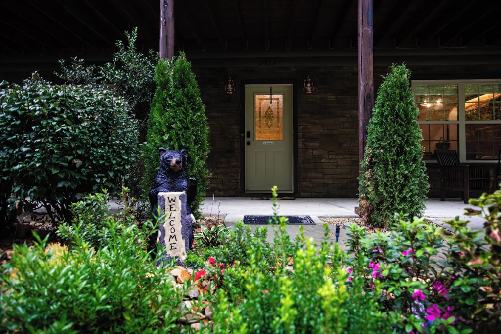 Pigeon Hills cabin entrance at night with bear welcome statue landscape lighting and garden